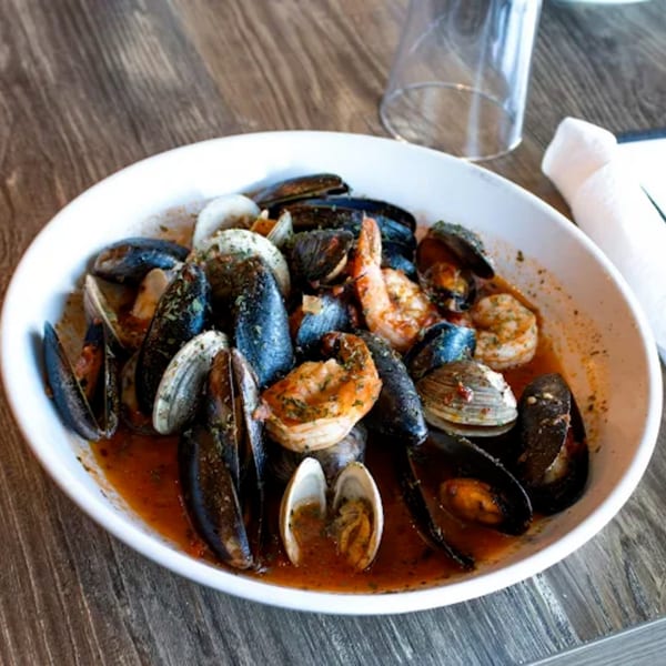 A white bowl of Viva Napoli's seafood pasta with mussels, clams, and shrimp in red sauce.