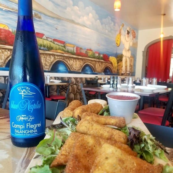 Fried mozzarella sticks and a bottle of Blue Naples wine on a table with a mural in the background.