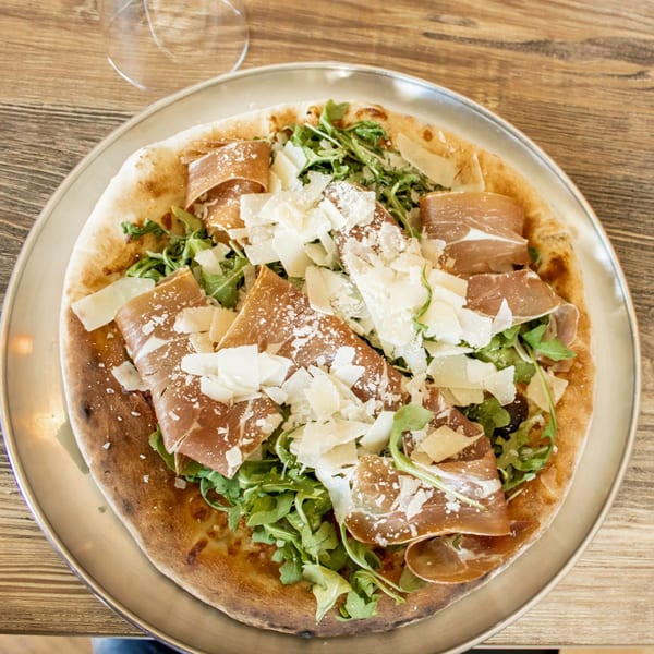 A Viva Napoli pizza with prosciutto, arugula, and shaved Parmesan on a metal tray.
