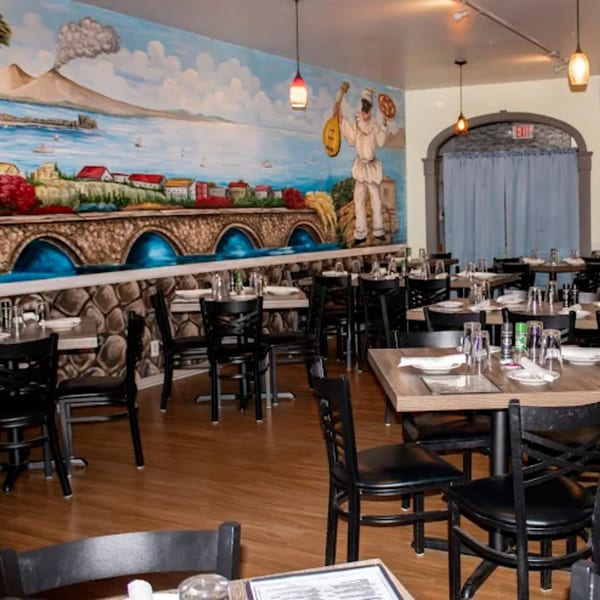 Viva Napoli Restaurant dining room with tables set, black chairs, and a large Italian mural.